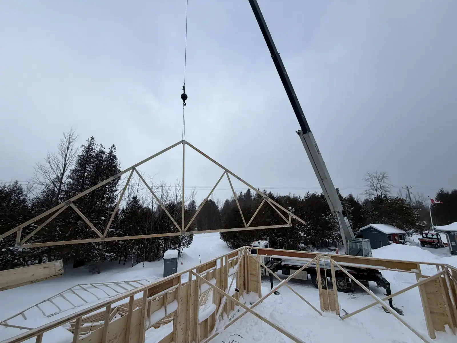 Crane lifting a roof truss on a winter jobsite