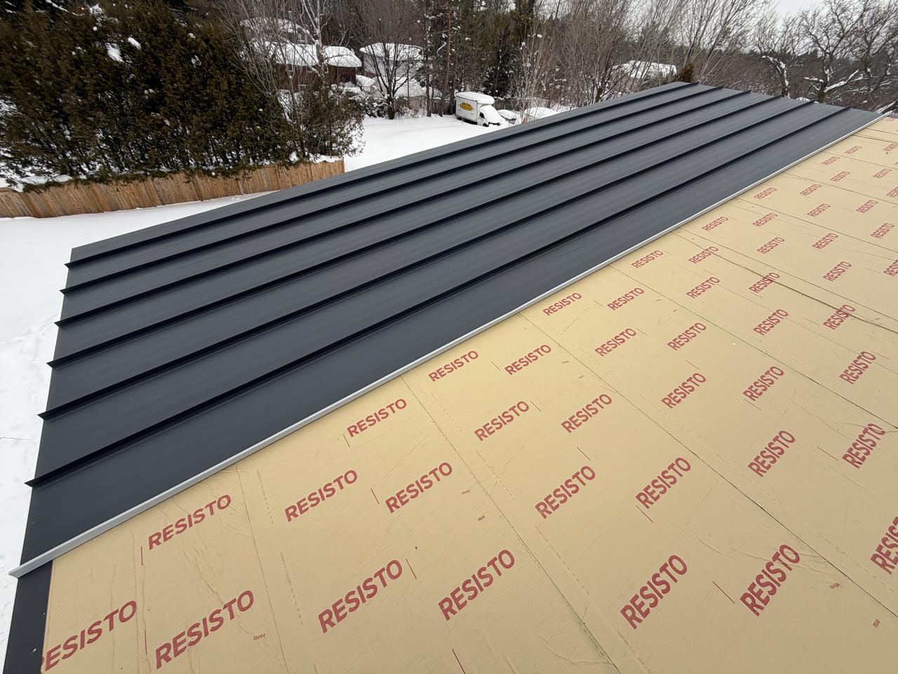 Matte charcoal standing seam panels being installed over high-temp underlayment