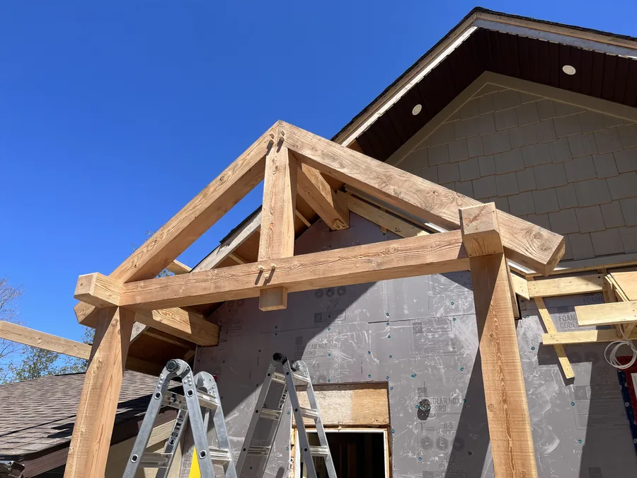 Timber frame roof being raised against a house on raising day